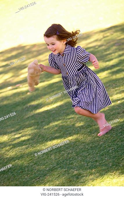park-scene, portrait, full-figure, 6-year-old girl wearing blue-white striped dress runs with her teddy in her hand bare-feeted over a green-yellow meadow  -...