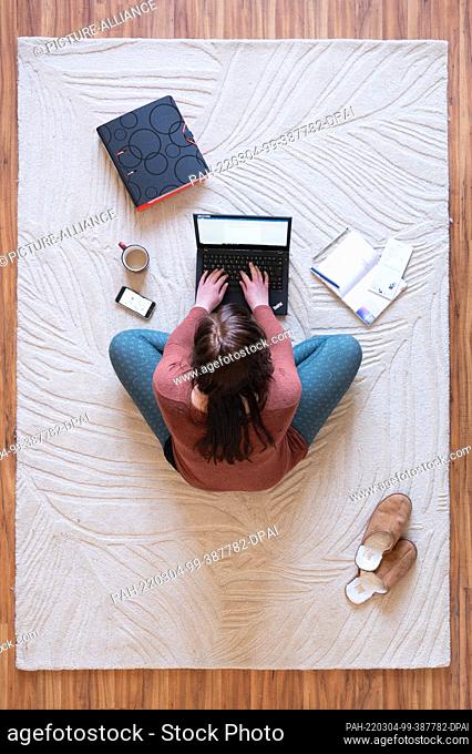 SYMBOL - 02 March 2022, Saxony, Dresden: A woman sits on a carpet in her home office and works on a laptop (posed scene)