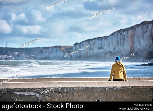Tourist admiring sea sitting on wall at vacation