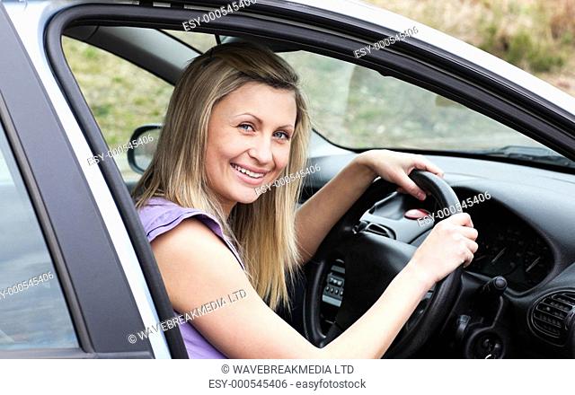 Happy female driver at the wheel sitting in her car smiling at the camera