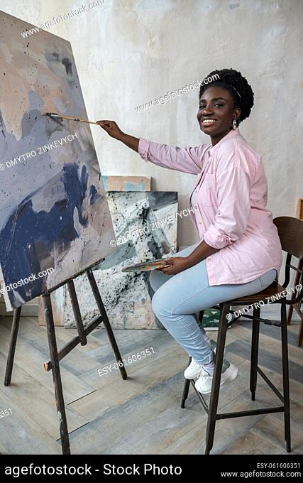 Artistry. A dark-skinned woman sitting near the easel and painting