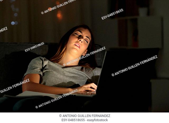 Tired woman sleeping on a couch beside a laptop in the night at home