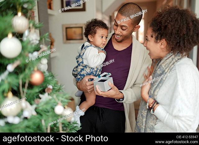 Happy parents and baby daughter opening Christmas gifts by tree