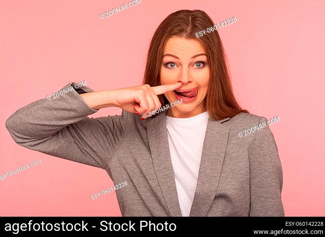 Portrait of funny young woman in business suit picking her nose, showing tongue out, removing boogers with comical wondered expression, bad habit