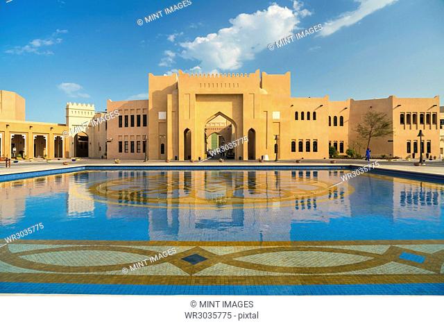 Facade of Middle Eastern building, pond with blue and golden mosaic tiles in foreground