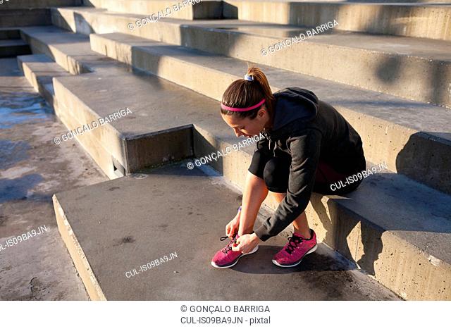Young woman tying shoelace on training shoe, stretching legs