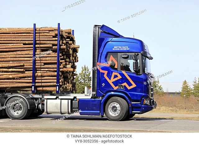 Side view of blue Scania R730 XT logging truck at speed on the road during Scania Tour Turku 2018 in Lieto, Finland - April 12, 2018