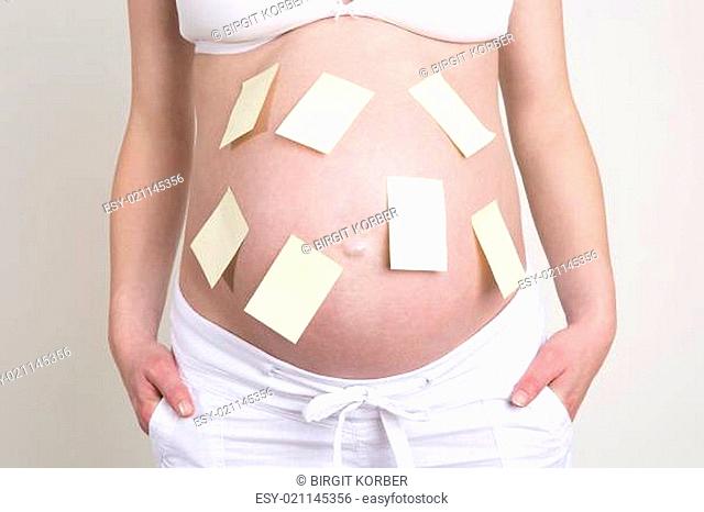 Pregnant woman with lots of yellow labels on her belly in front of beige background