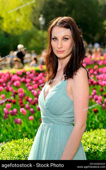 A beautiful young Russian woman in a park in the first warm spring sun with a light turquoise dress