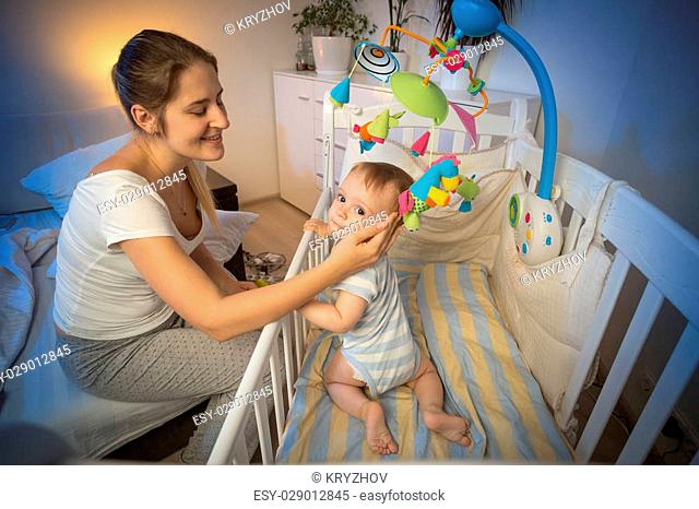 Portrait of happy young mother looking at her baby in crib before going to sleep