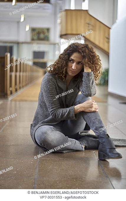 thoughtful, multi-cultural mature woman sitting on floor in christian church. Half German and half Turkish ethnicity. In Munich, Germany