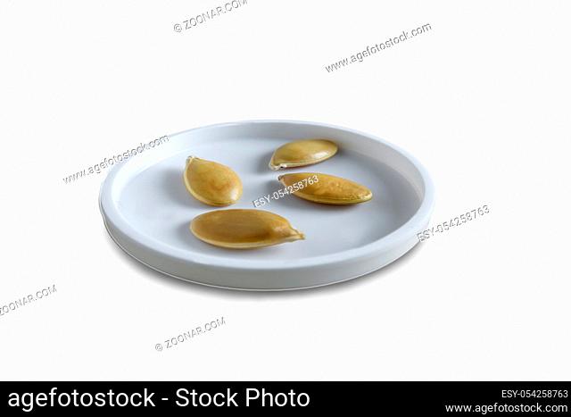 On a white saucer large pumpkin seeds. Presented on a white background