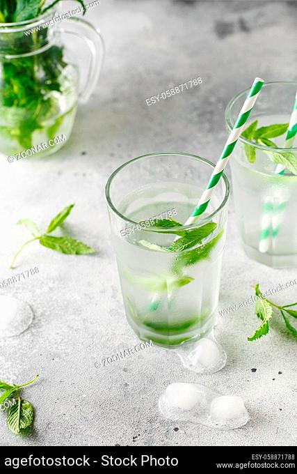 glasses of cold water with fresh mint leaves and ice cubes on grey concrete background. Food photography