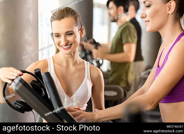 Young woman helping her friend to set the time, speed and incline of the next running session on treadmill