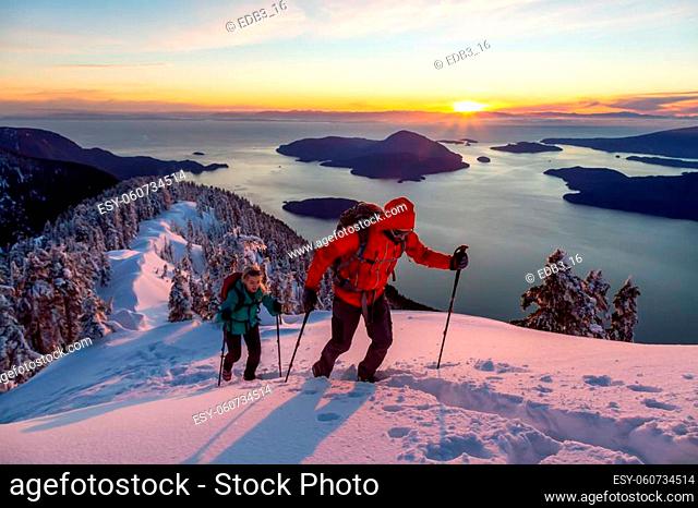 Adventure seeking man and woman are hiking to the top of a mountain during a vibrant winter sunset. Taken in Mnt Harvey, North of Vancouver, BC, Canada