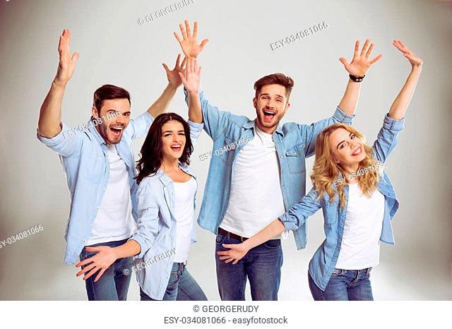 Beautiful young people in jeans are happy and playful, stretching hands, looking at camera and smiling, on a gray background