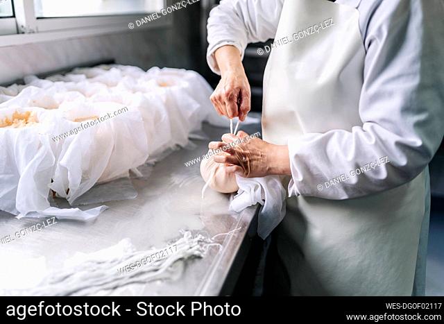 Skilled chef wrapping cheese in cloth at factory