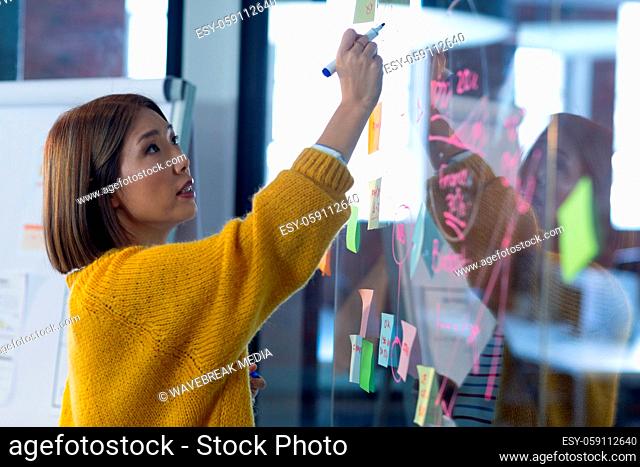 Asian businesswoman standing in front of glass wall and writing in office