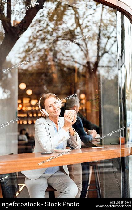 Businesswoman holding coffee cup enjoying music listening through wireless headphones in cafe