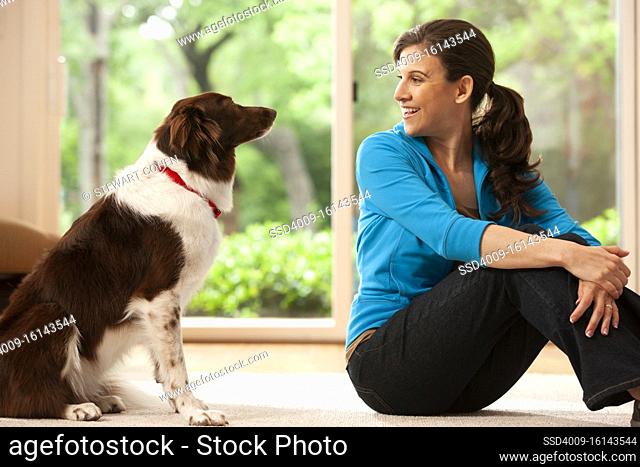 woman at home on rug in living room with pet dog looking at each other, view of back yard through double sliding door