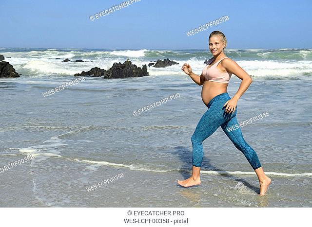 Smiling pregnant woman jogging on the beach