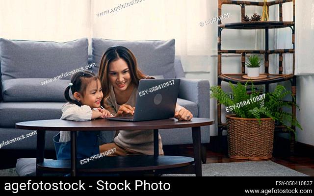 Asian young mother with laptop computer teaching her kid to learn or study online in living room at home, Mum and little preschool daughter learning online on...