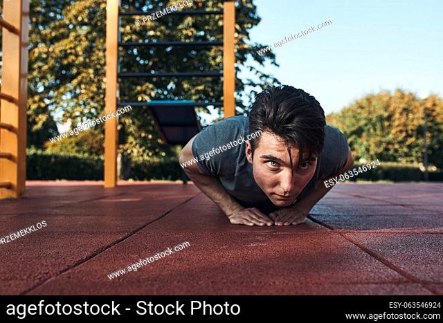 Young man doing push-ups on a red rubber ground during his workout in a modern calisthenics street workout park. Man wearing sportswear looking away