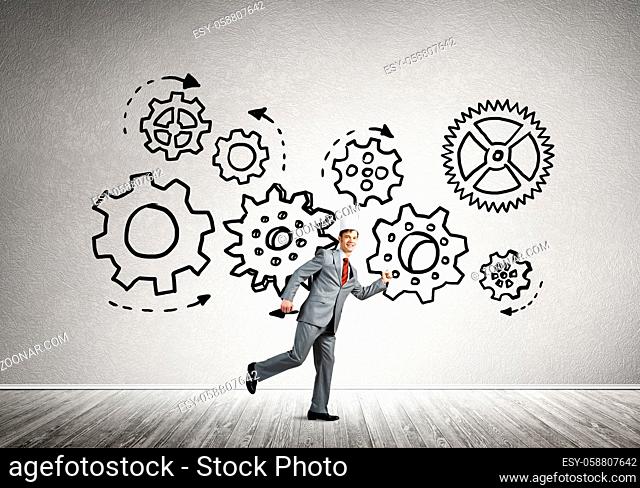 Young handsome businessman wearing white paper crown running and gear mechanism on wall