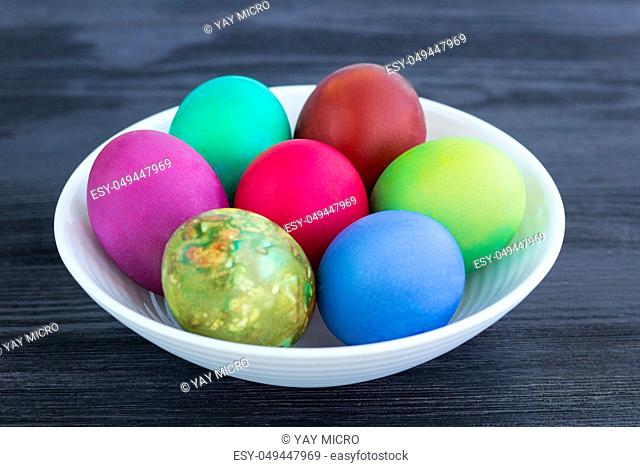 White plate of Easter multicolored boiled eggs decoration on black wooden background