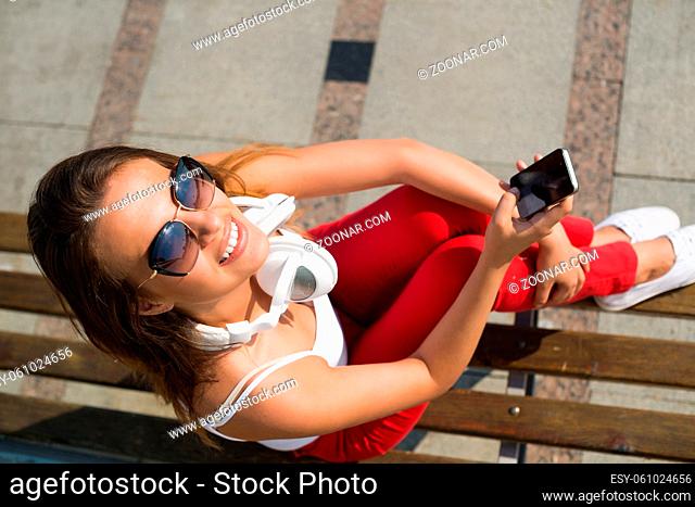 Top view of young pretty brunette with mobile phone sitting on bench in summer park