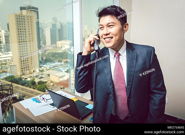 Portrait of happy businessman talking on telephone in the office