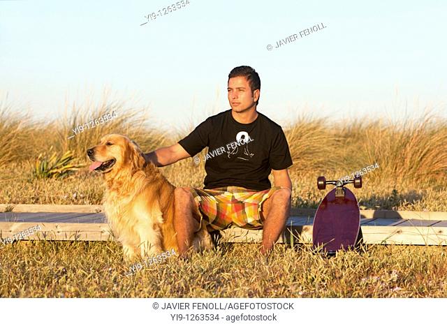 Young Male posing with his skate board and his dog