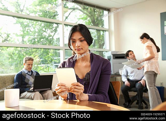 Young woman sitting at a table in an office breakroom working on a tablet