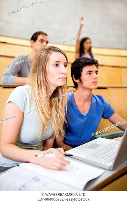 Portrait of students listening a lecturer while their classmate is raising her h