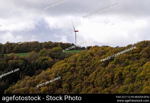 PRODUCTION - 04 November 2022, Rhineland-Palatinate, Monreal: A single wind turbine towers behind a wooded hill near the village of Monreal
