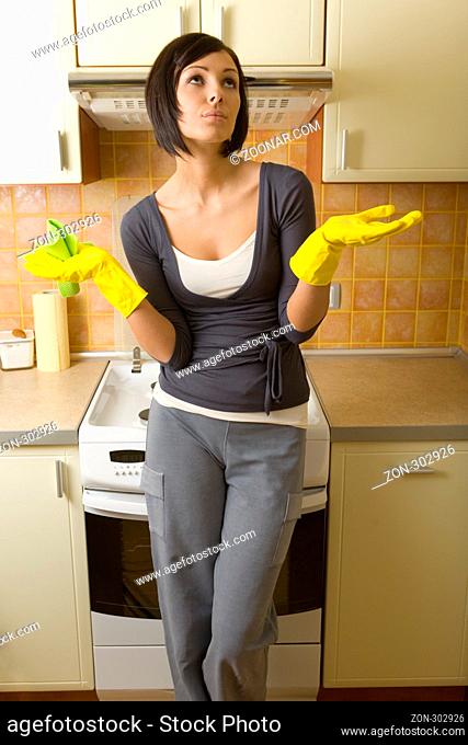 Young woman in yellow rubber gloves. She's standing back at cooker with raised hands. She's looking up. Front view