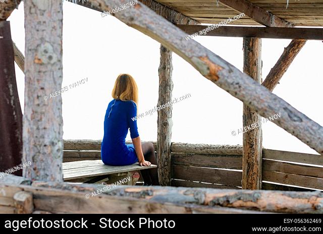 A girl sits on a table in a gazebo from a log house