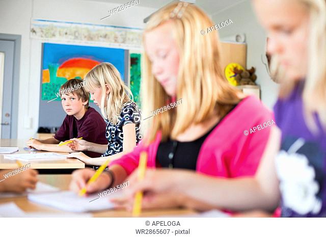 Portrait of serious schoolboy sitting at desk in classroom