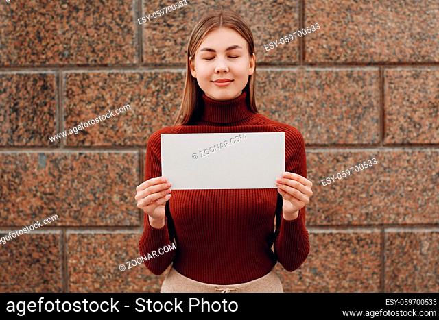 Girl holds white paper in hand stone background. Young woman with white blank template sheet with empty space