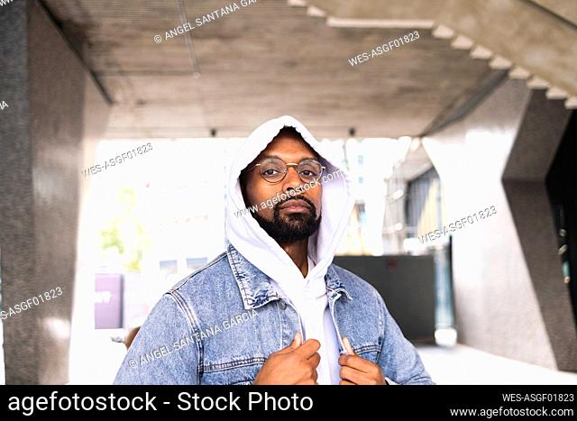 Man with hooded shirt and denim jacket outside building