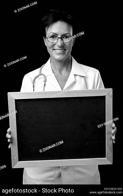 Studio shot of mature beautiful Scandinavian woman doctor with short hair against black background in black and white