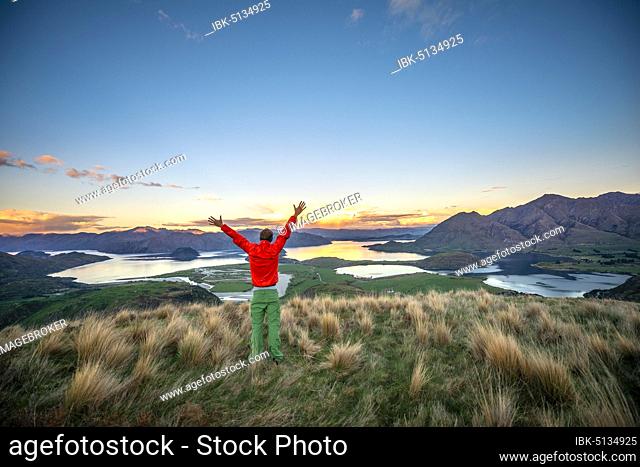Hiker stretches his arms in the air, panoramic view of Wanaka Lake and mountains at sunset, Rocky Peak, Glendhu Bay, Otago, South Island