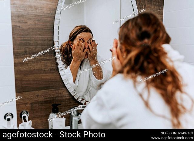 Woman washing her face in front of mirror