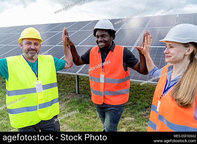 Smiling multiracial engineers giving high five to each other at solar power station