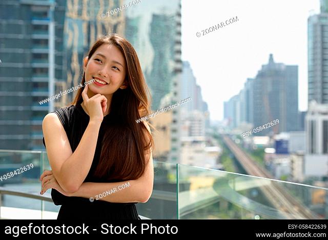 Portrait of young beautiful Asian businesswoman against view of the city