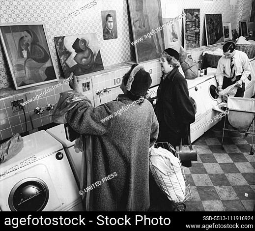 Dividing his time between art work and soap suds, Pernicone attends to his laundry business in background as his customers admire the paintings propped against...