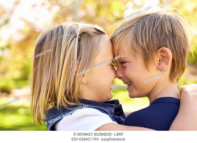 Young brother and sister nose to nose in a park, side view