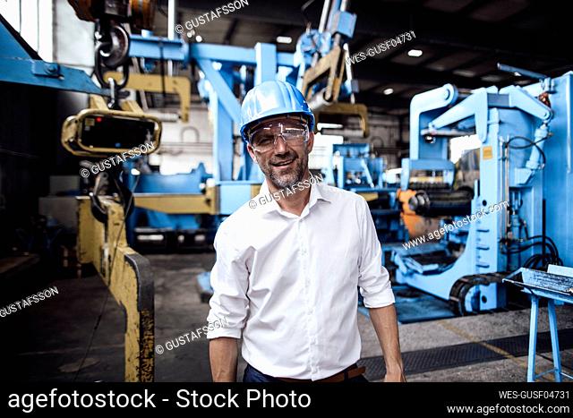 Smiling businessman wearing protective eyewear while standing in industry