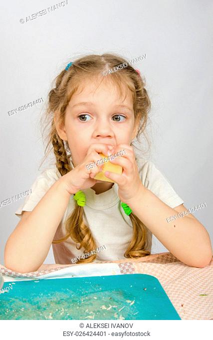 Six-year girl with pigtails trying to bite off a piece of cheese that keeps both hands