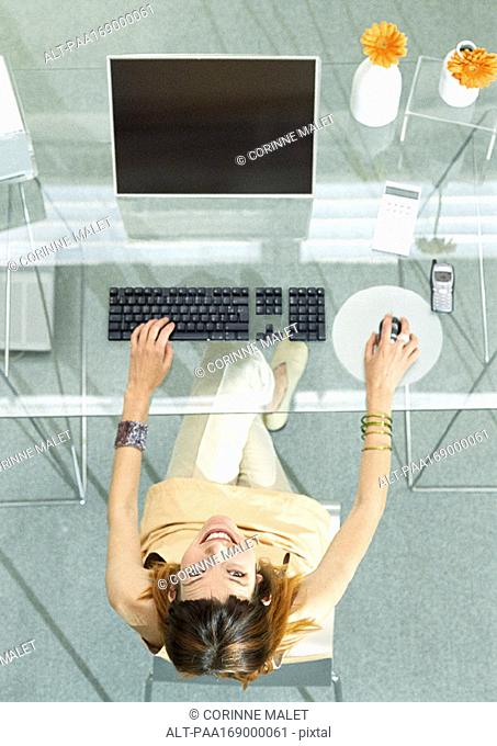 Woman at table with screen and keyboard, high angle vew